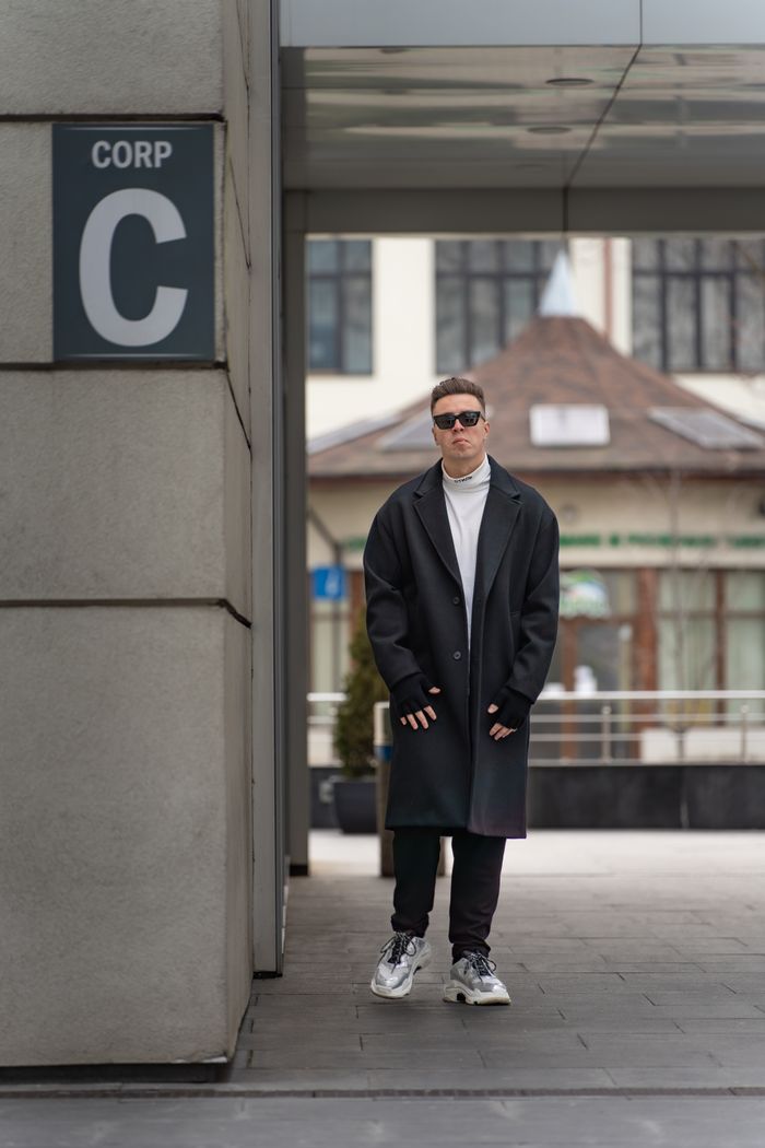 Stylish man in overcoat stands confidently on a modern city street, embodying urban fashion.
