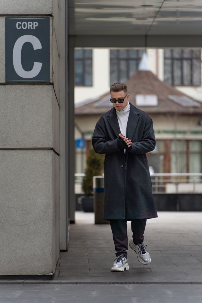 Stylish young man in a long coat walking on a city street, exuding modern urban fashion.